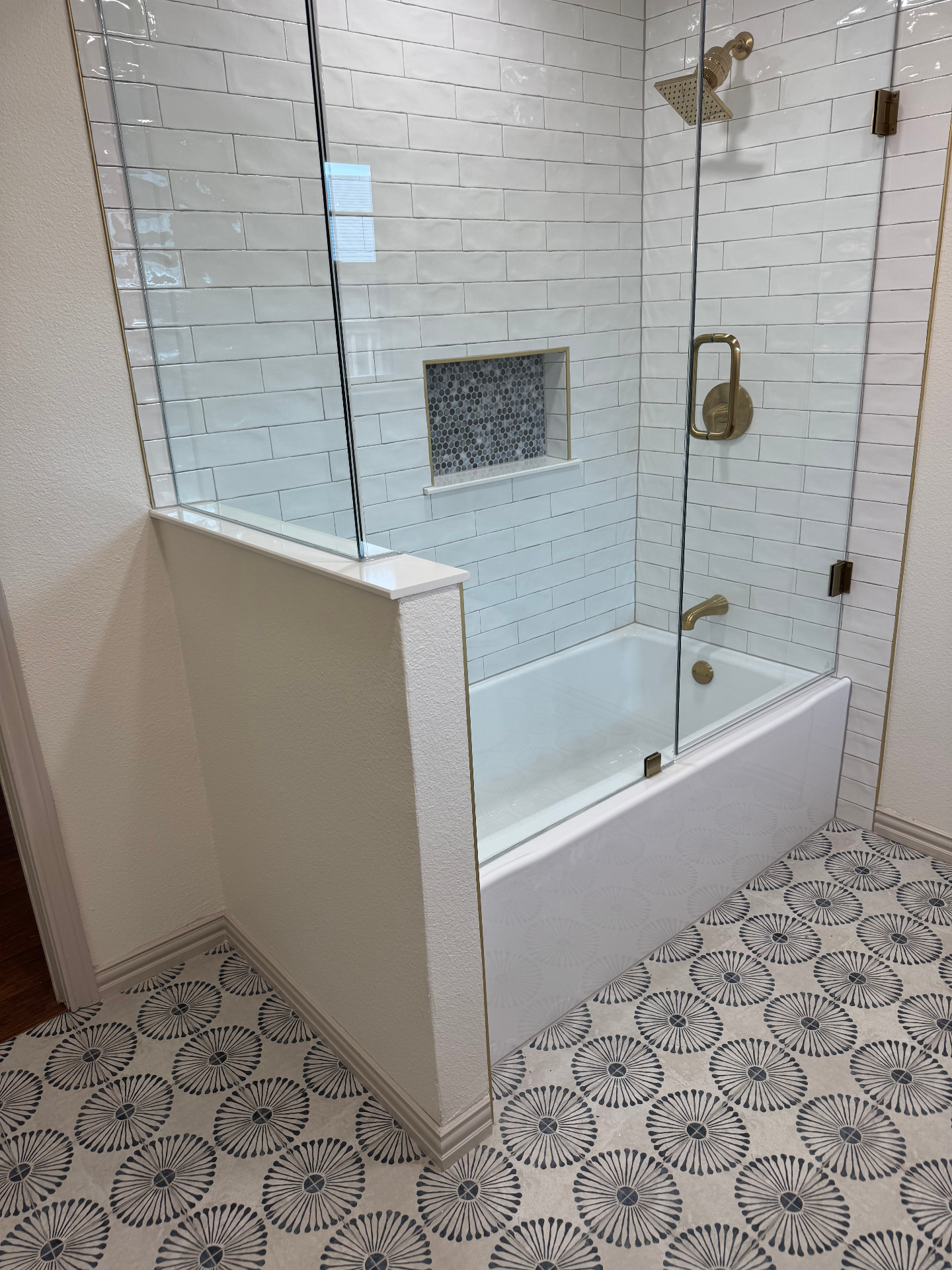 Finished bathroom tub with glass enclosure, brass fixtures, and patterned tile floor