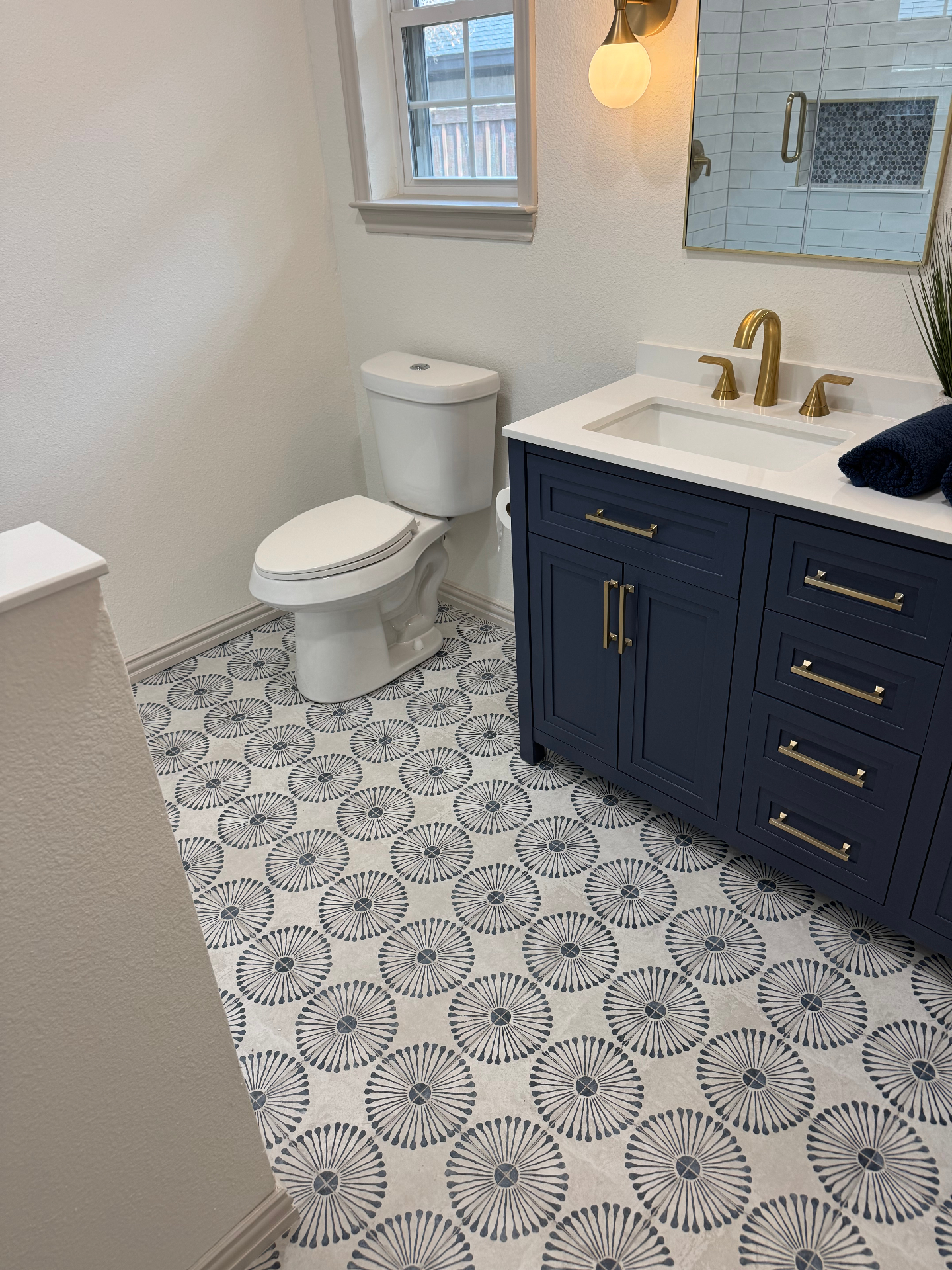 Finished bathroom with navy vanity, brass fixtures, and patterned tile floor