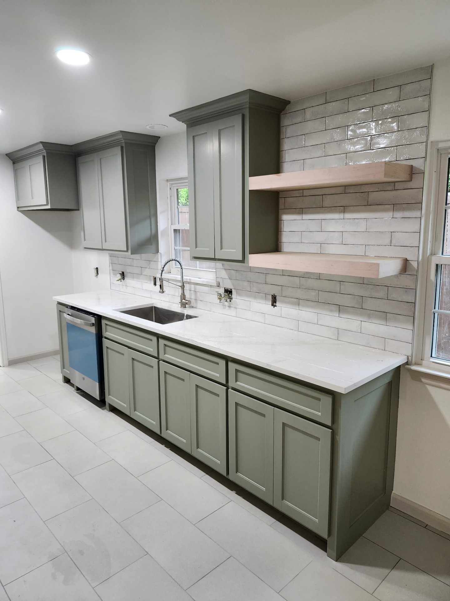 Finished kitchen with sage cabinets, open wood shelving, and white tile backsplash