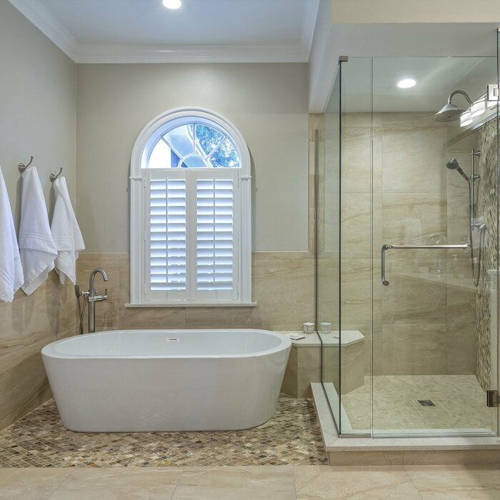 Luxury bathroom with arched window, freestanding tub, and glass shower