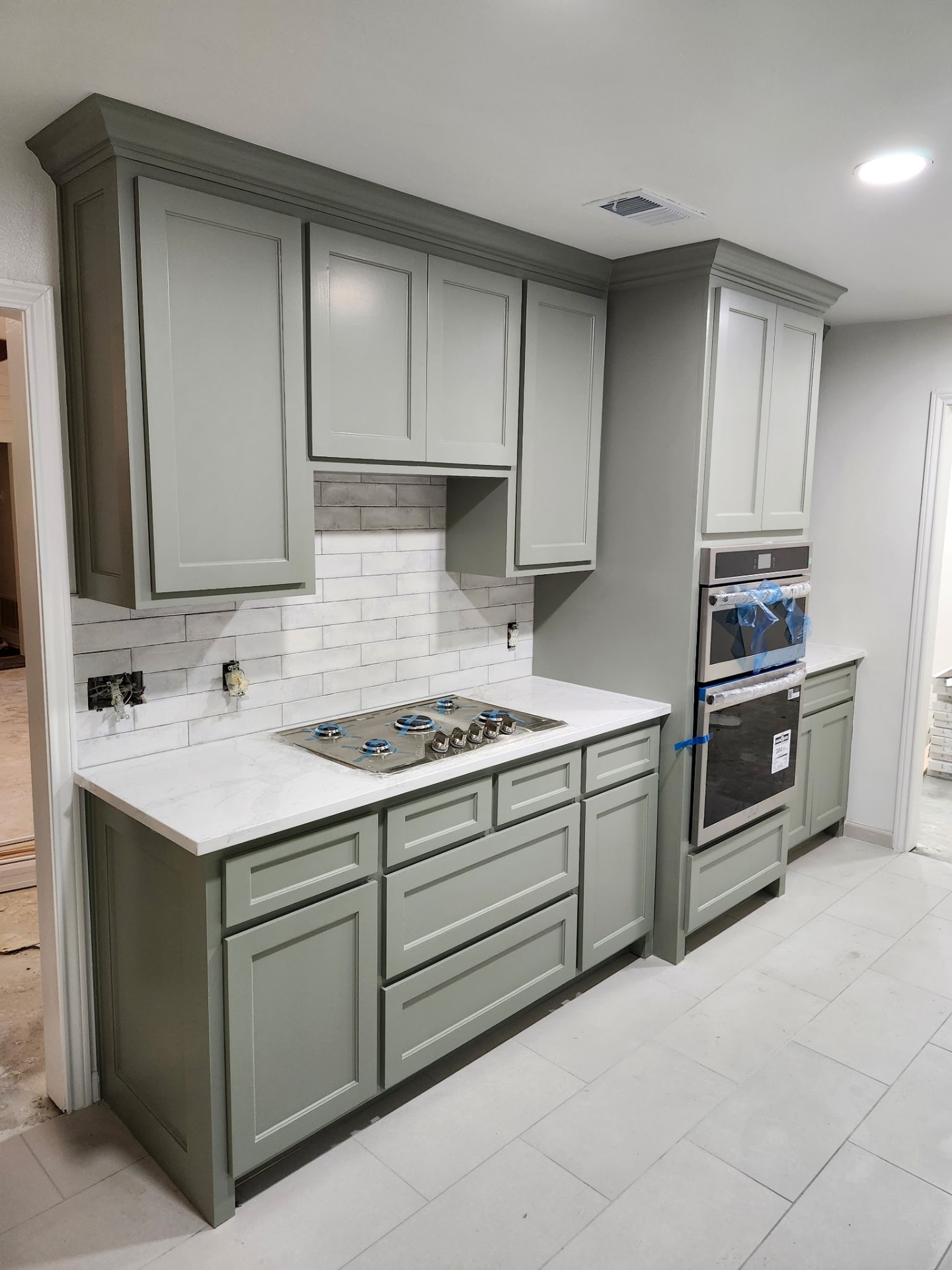 Finished kitchen cooktop wall with built-in ovens and custom sage cabinetry